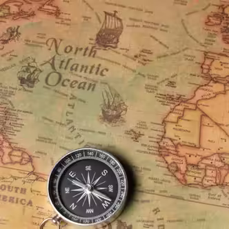 A compass on laid on top of a map of the Atlantic Ocean.